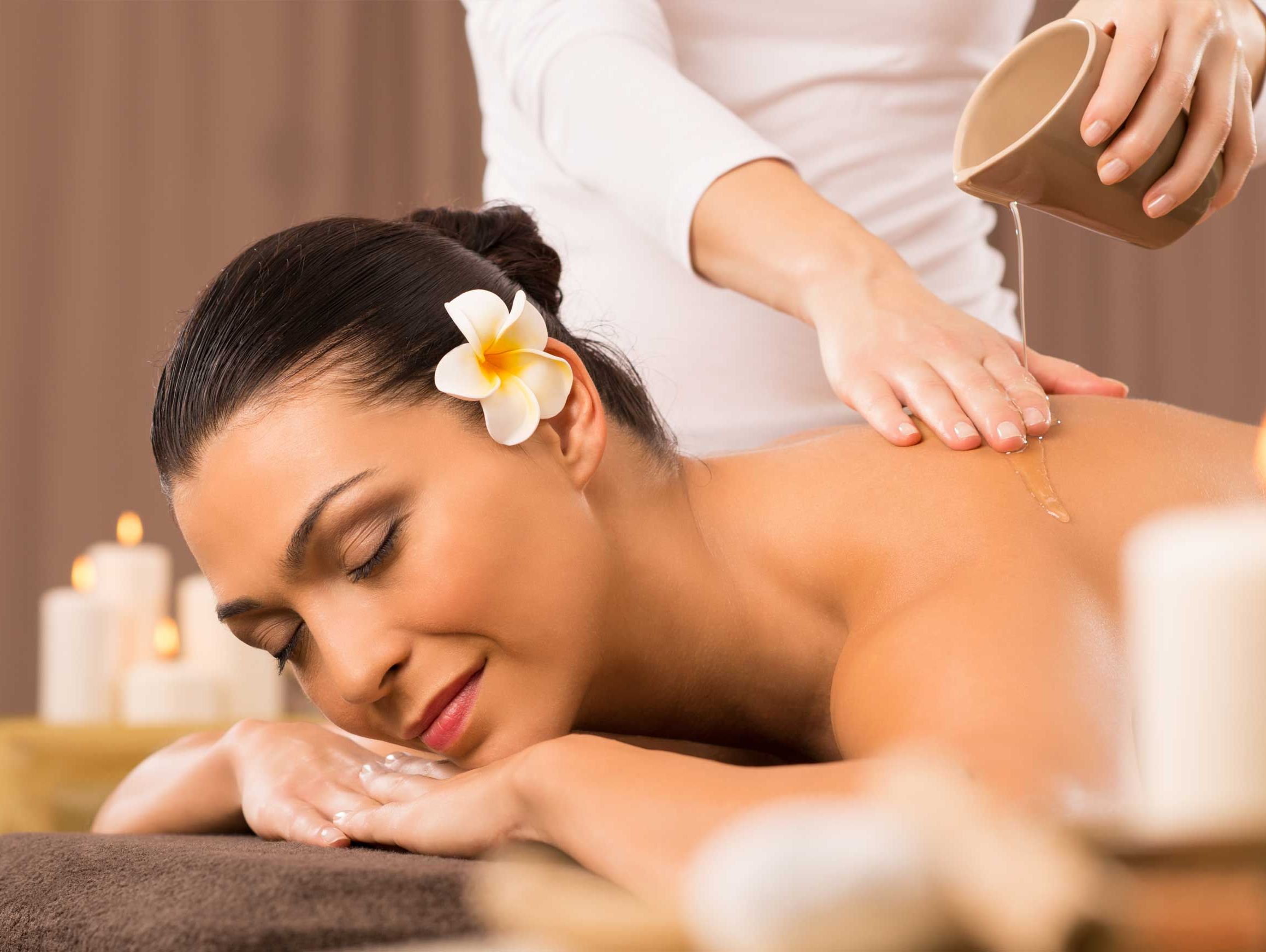 “Kvinna som får oljemassage av professionell massör, omgiven av levande ljus och lugn atmosfär.