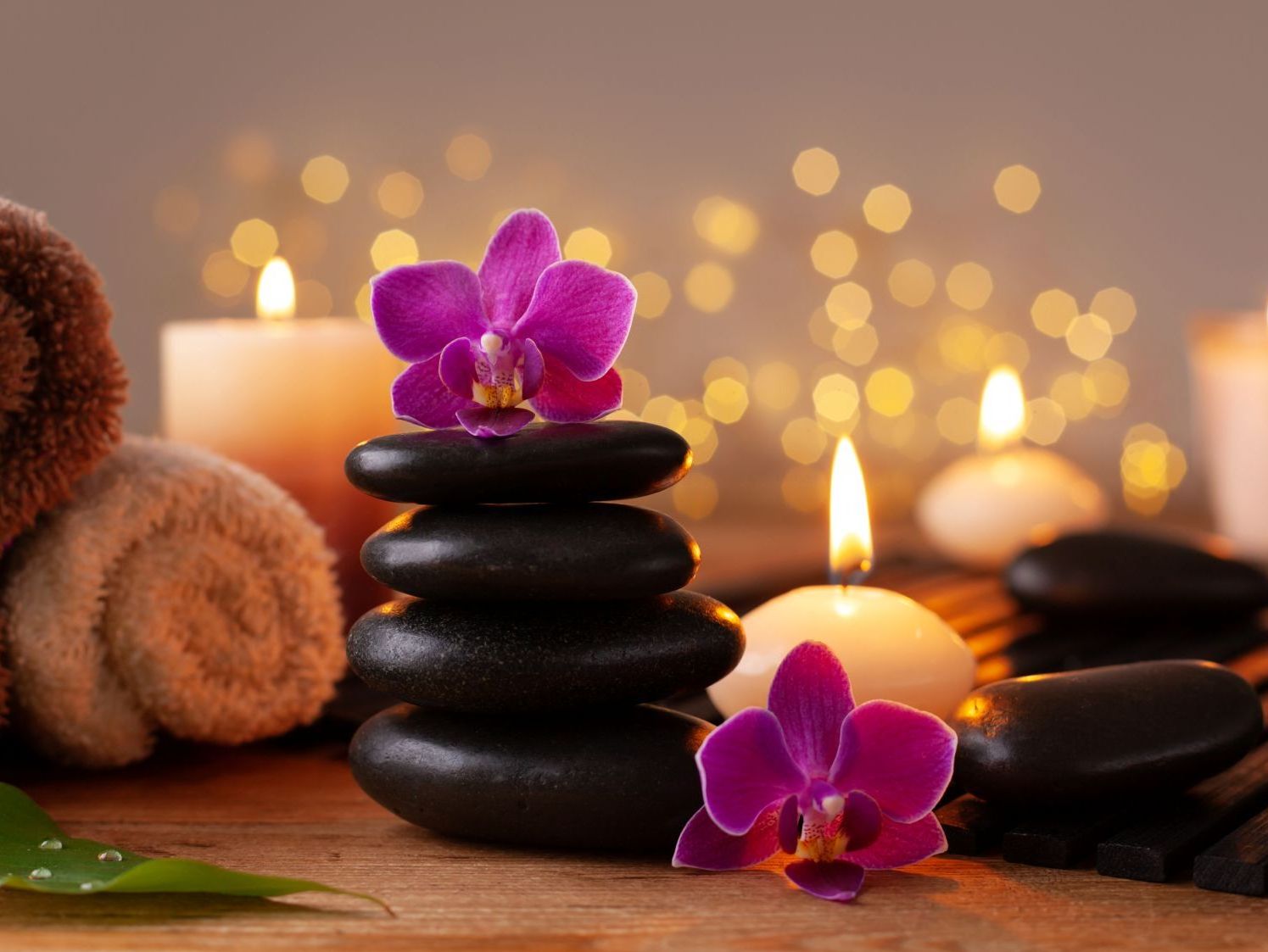 Avslappnande spa-miljö med varma stenar, handdukar och orkidéblommor i ljuslyktors sken hos Suai Massage i Gävle.